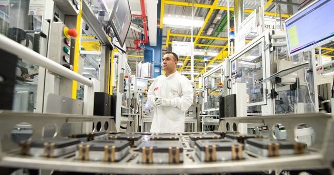 A skilled worker standing in front of a batch of radar sensors destined for the automotive industry